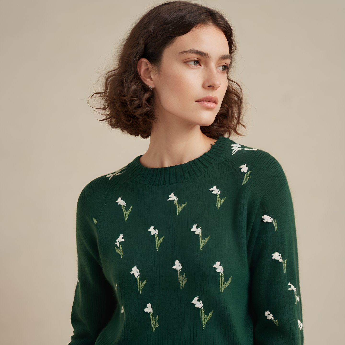 Product shot, Soft knitwear sweater that is dark green that has a white lily of the valley on it. The background is sunny and it is a product shot